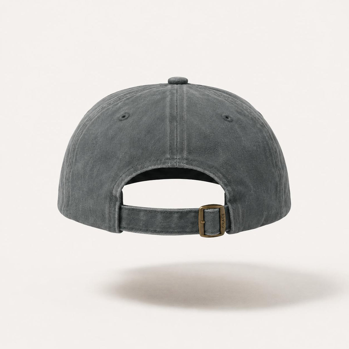 The back view of a washed charcoal gray baseball cap with an adjustable strap and a bronze-toned metal buckle, shown against a light off-white background.