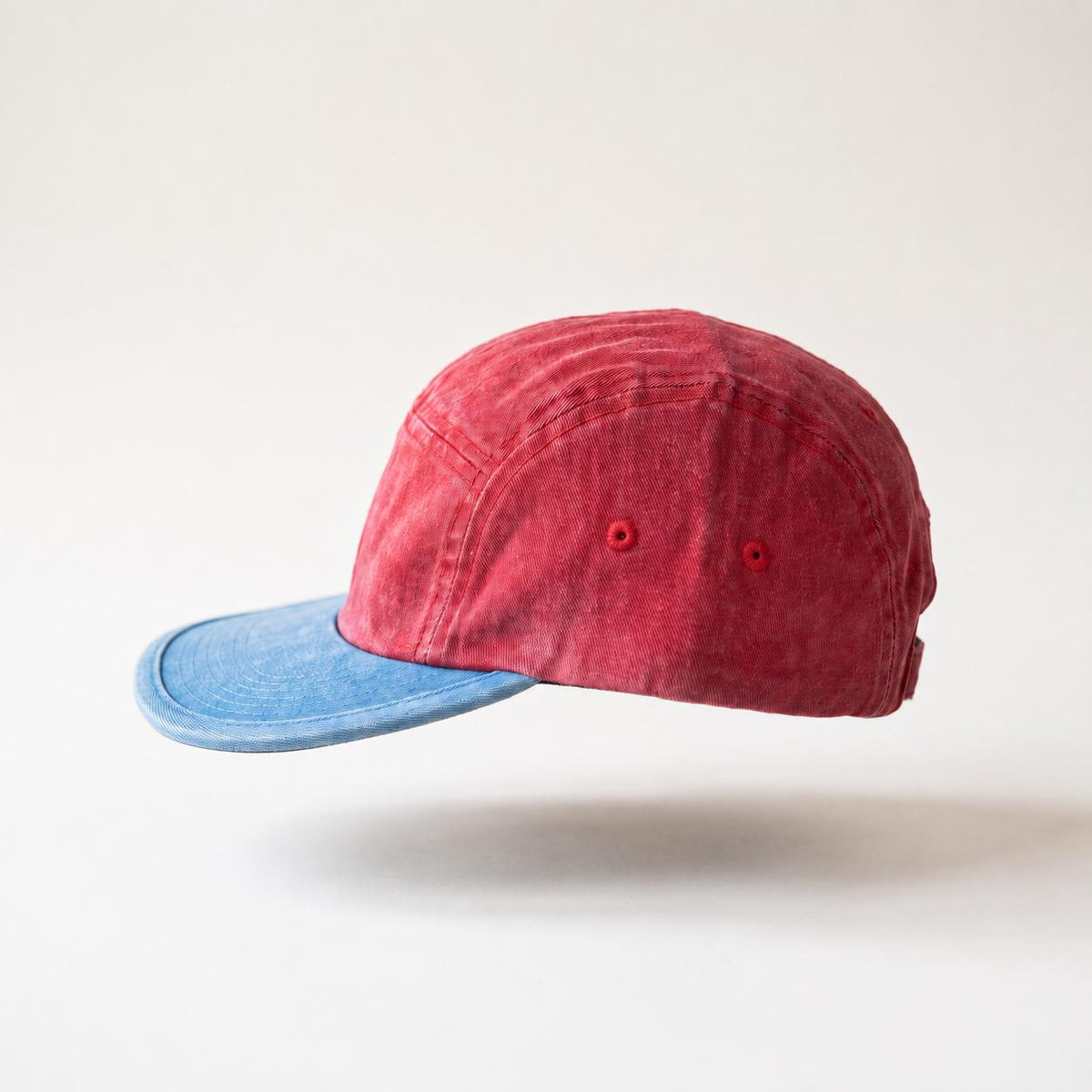 A red washed cotton 5-panel cap with a contrasting light blue denim visor, shown floating against a clean white background.