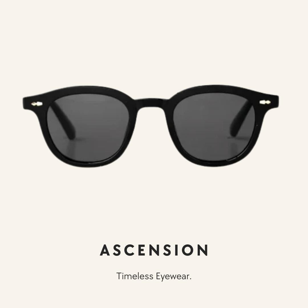 Black round-frame sunglasses with dark lenses and small gold accents on the temples, shown against a light beige background with the brand name ASCENSION and the tagline 'Timeless Eyewear.' below.