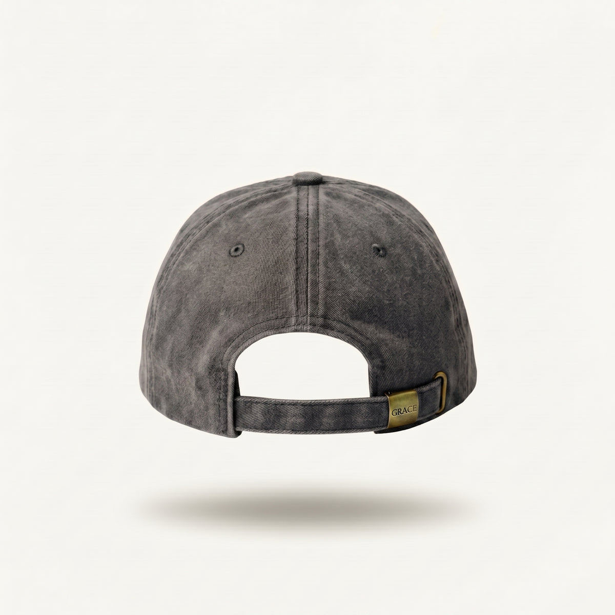 A dark gray washed cotton baseball cap shown from the back, featuring a small gold brand tag on the back strap, set against a clean off-white background.