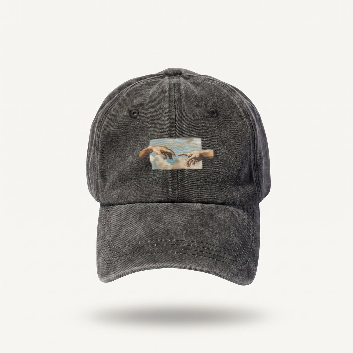 A dark gray washed cotton baseball cap featuring a rectangular patch on the front depicting Michelangelo's Sistine Chapel ceiling with God's hands reaching toward two birds.