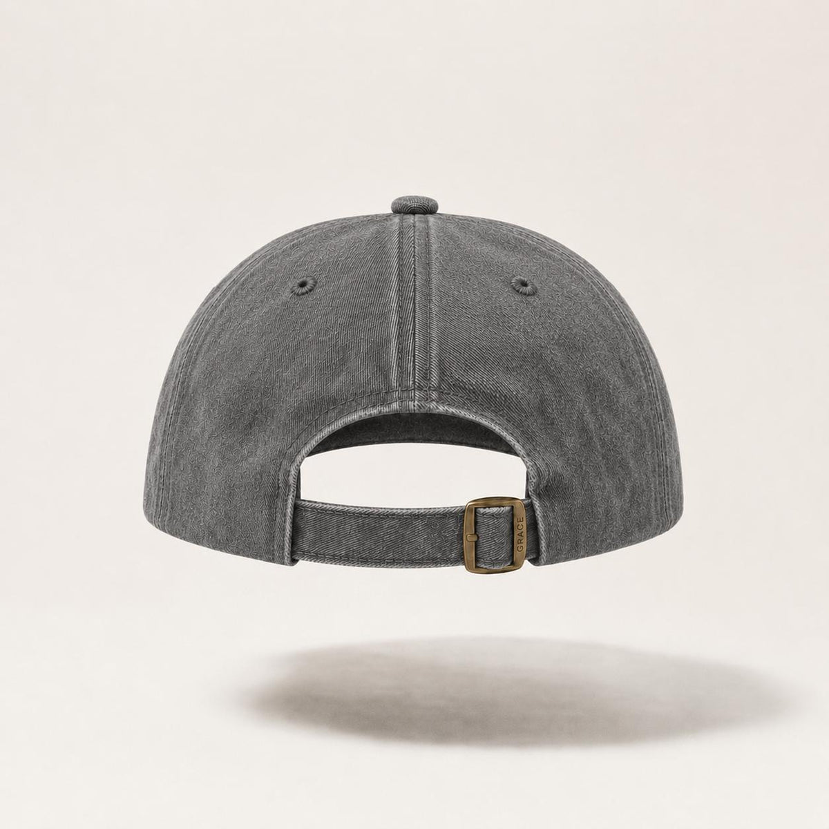 A dark gray washed cotton baseball cap shown from the back, featuring a matching fabric strap and a bronze-toned metal buckle, set against a light beige background.