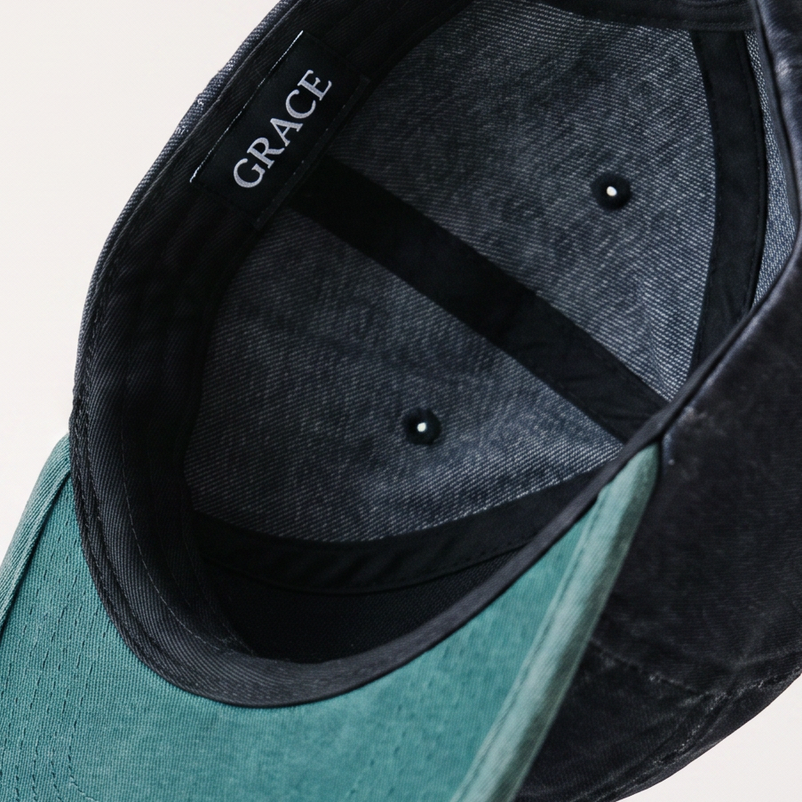 A dark navy blue baseball cap with a teal-green curved brim, shown floating against a light off-white background. The brand name 'GRACE' is visible on the inner side of the crown.