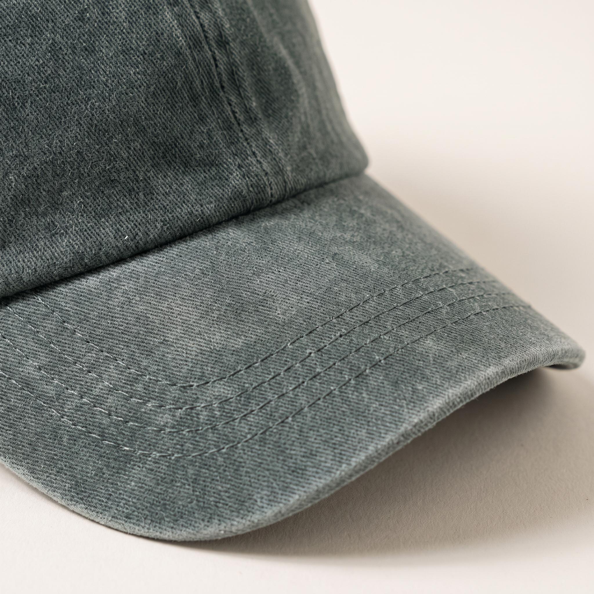 Close-up of a washed dark gray baseball cap showing the fabric texture and curved brim on a light beige background.