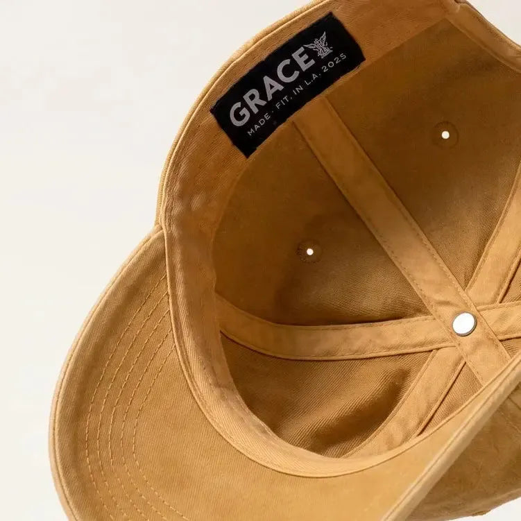 A tan suede baseball cap shown floating at an angle, displaying the interior crown with a black 'GRACE' brand label and metal ventilation eyelets.
