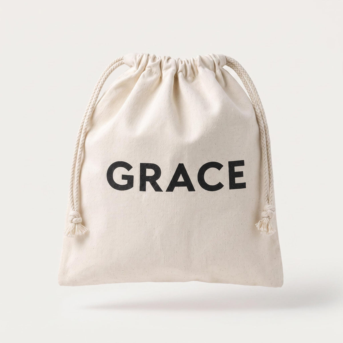 A small off-white canvas drawstring pouch with the word 'GRACE' printed in bold black capital letters on the front, shown against a light gray background.