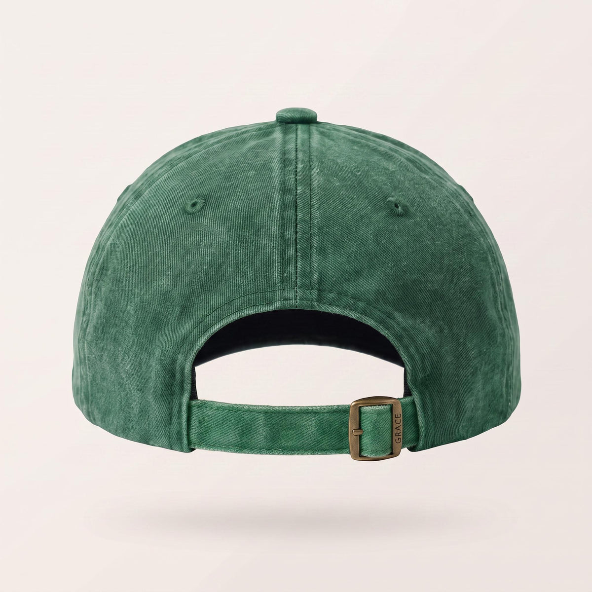 The back view of a washed green baseball cap with an adjustable strap and a bronze-tone metal buckle, shown on a light beige background.