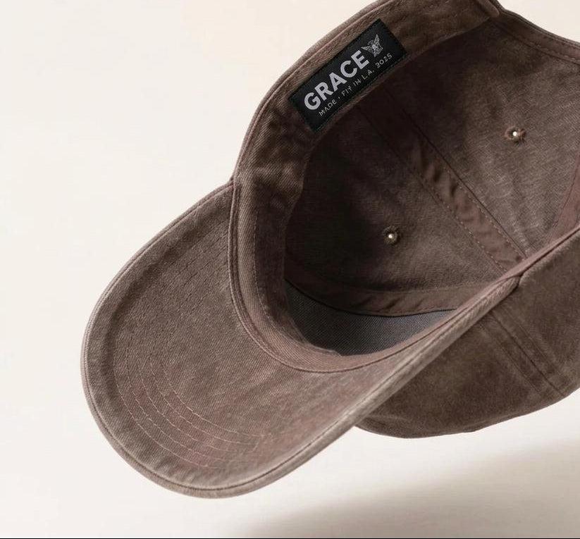 A dark brown washed cotton cap shown from an angled top-down perspective, highlighting the interior lining and a black brand label that reads 'GRACE'.