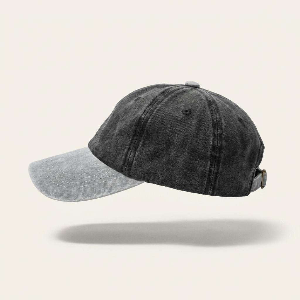 A washed black baseball cap with a contrasting light gray brim, shown floating against a solid off-white background with a soft shadow underneath.