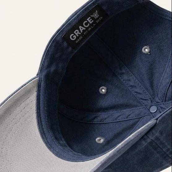 A navy blue cotton baseball cap shown from an angled top-down perspective, featuring a light gray visor underside and a black interior label with the brand name 'GRACE'.