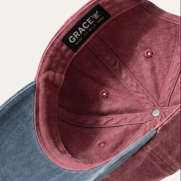 A dual-tone baseball cap with a dusty rose velvet crown and a blue denim-look curved brim, shown floating against a light beige background. The inside of the crown features a black brand label reading 'GRACE'.