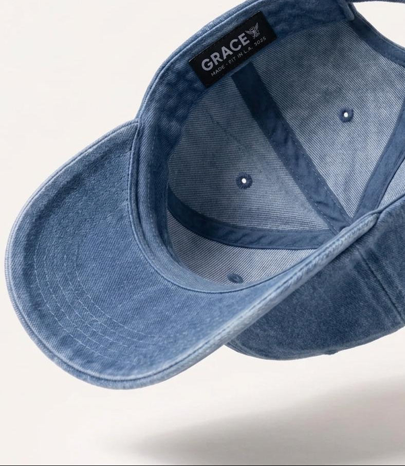 A blue denim baseball cap shown floating at an angle, displaying the interior with a black brand label that reads 'GRACE' and 'MADE IN THE USA'.