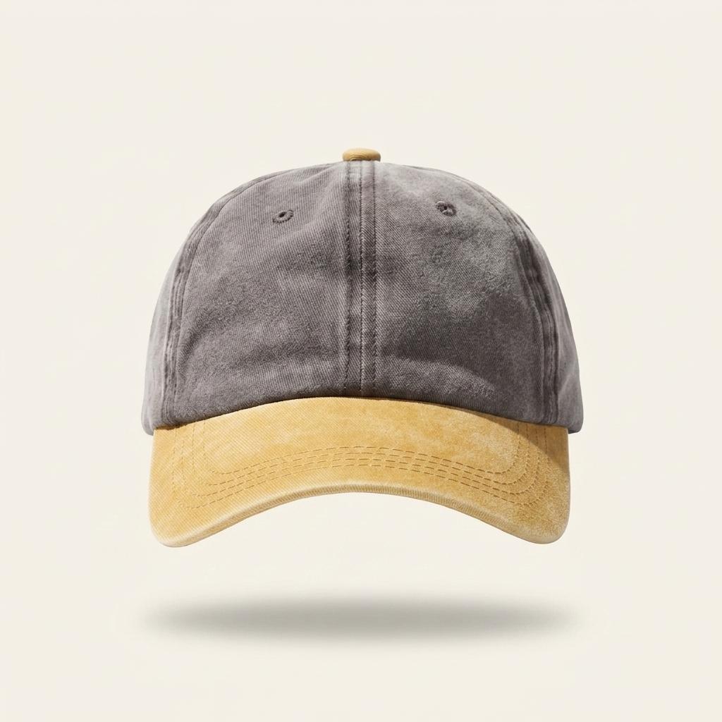 A two-tone baseball cap with a washed dark gray crown and a mustard yellow brim, shown against a light beige background.