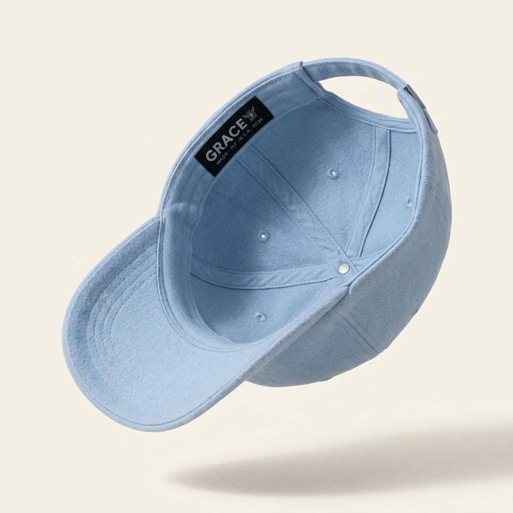 A light blue cotton baseball cap shown floating at an angle, displaying the interior with a black brand label that reads 'GRACE'.