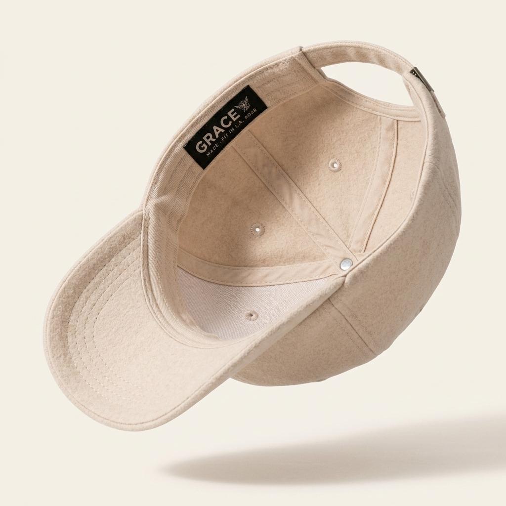 A light beige baseball cap shown from an angled top-down perspective, featuring a black interior label that reads 'GRACE CLOTHING CO.' on a clean, solid off-white background.