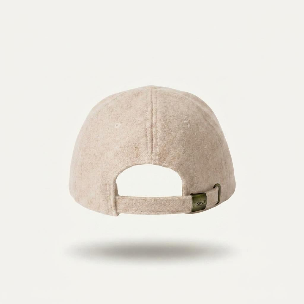 A light beige felt baseball cap shown from the back, featuring a curved strap closure with a small olive green tag, set against a solid off-white background.