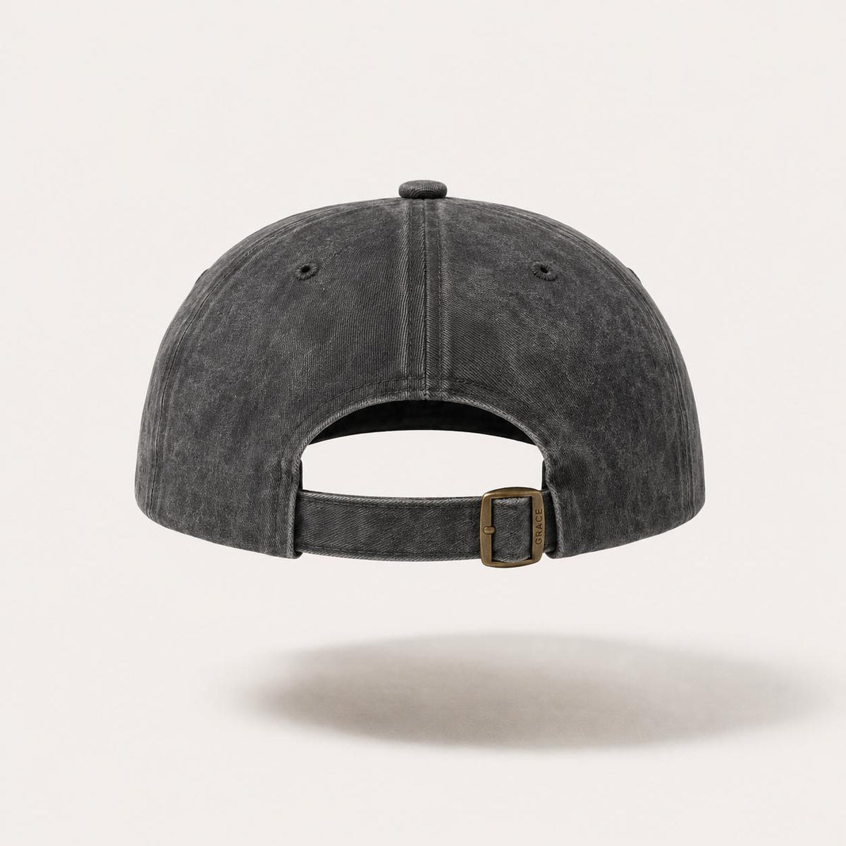 A dark gray washed cotton baseball cap shown from the back, featuring a curved strap and a small gold-tone metal buckle, set against a light beige background.