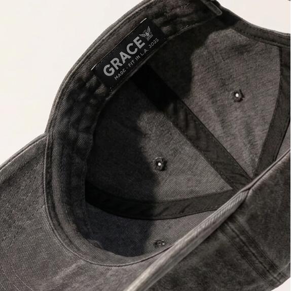 A dark gray washed cotton baseball cap floating at an angle against a clean white background, showing the curved brim, interior crown, and adjustable strap.