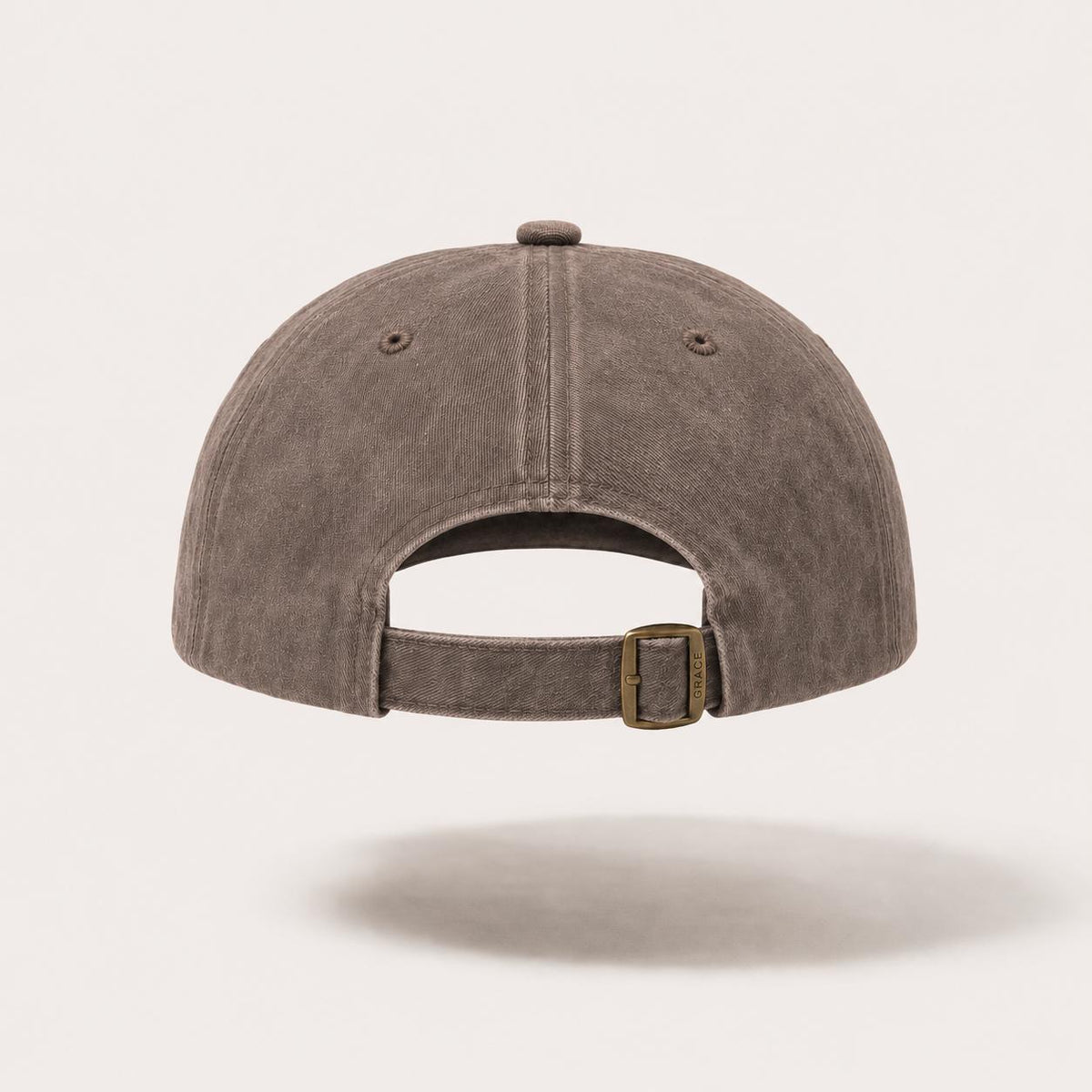 A washed dark brown baseball cap shown from the back, featuring a curved back strap with a brass-tone buckle, set against a light off-white background.