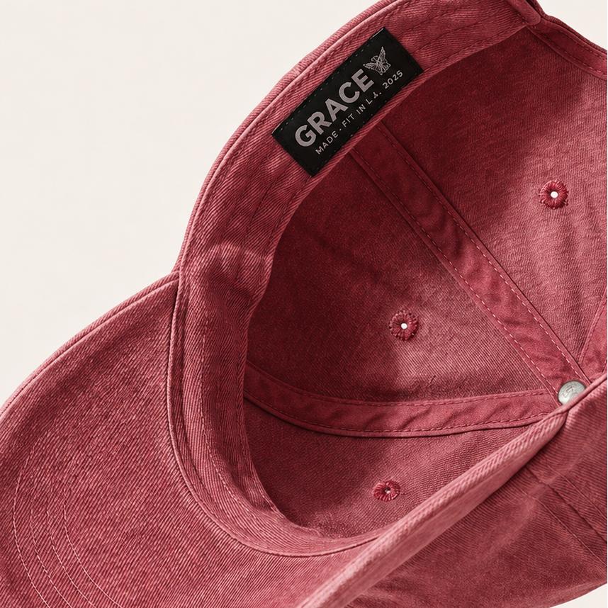 A dusty rose pink cotton baseball cap shown from an overhead angle, featuring a black interior label with the brand name 'GRACE' and a light beige background.
