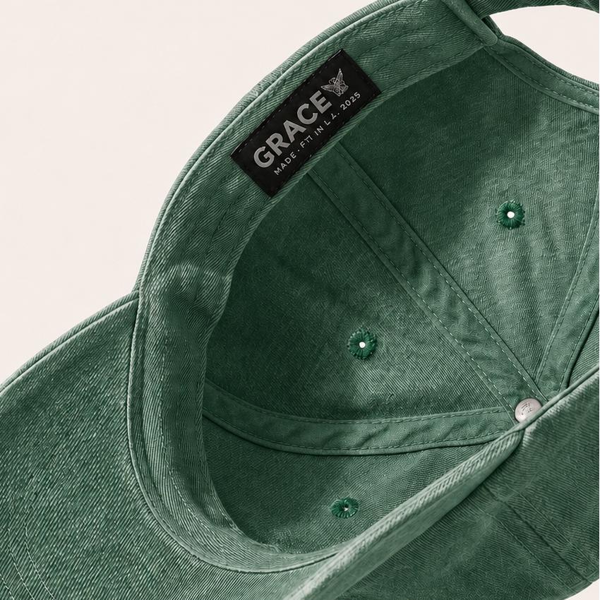 A dark green washed cotton baseball cap shown from an angled top-down view, featuring a black interior label with the brand name 'GRACE'.