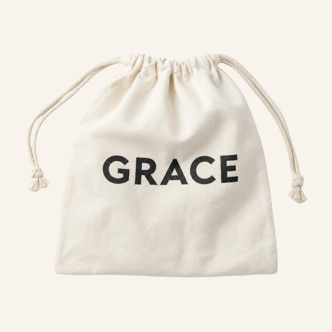 An off-white cotton drawstring pouch with the word 'GRACE' printed in bold black letters on the front, set against a solid off-white background.
