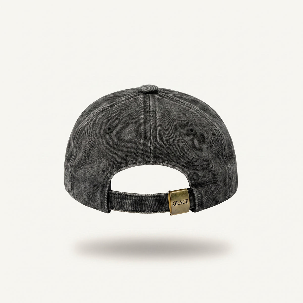 A dark gray acid-wash baseball cap shown from the back, featuring a small gold-tone metal brand tag that reads 'GRACE' on the adjustable strap, set against a light off-white background.