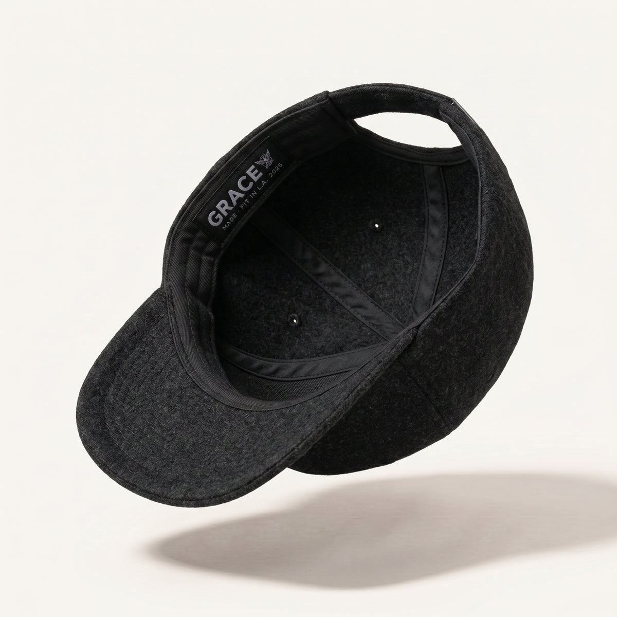 A black felt baseball cap shown floating at an angle, displaying its curved brim, black interior, and a visible GRACE brand label on the side, set against a clean off-white background with a soft shadow.