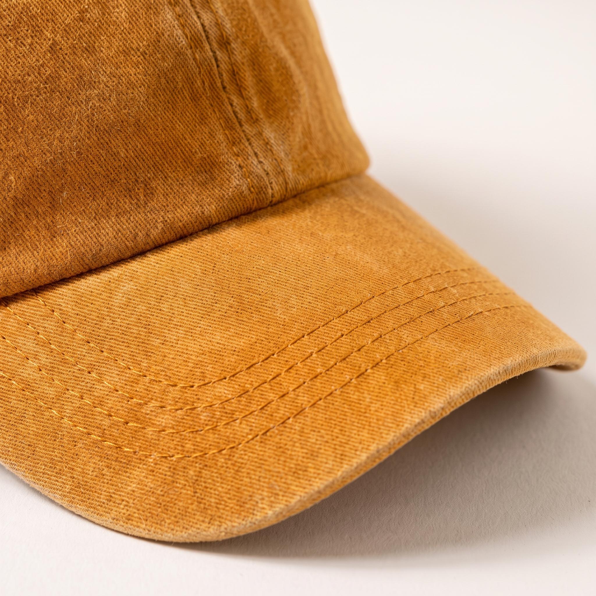 A close-up shot of a washed mustard yellow baseball cap, showing the fabric texture and curved brim against a plain light background.