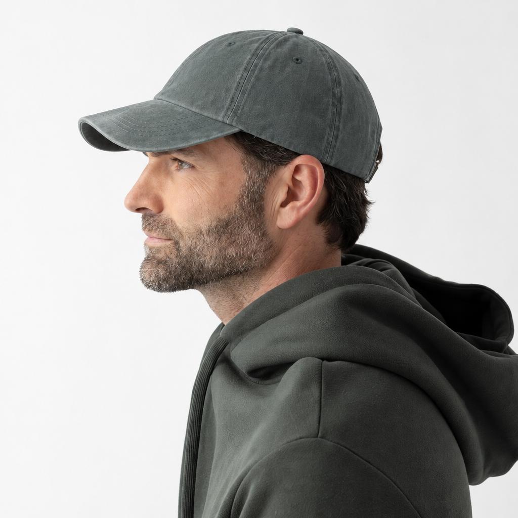 A man in profile wearing a dark gray washed baseball cap and a matching dark gray hoodie, photographed against a clean light gray studio background.