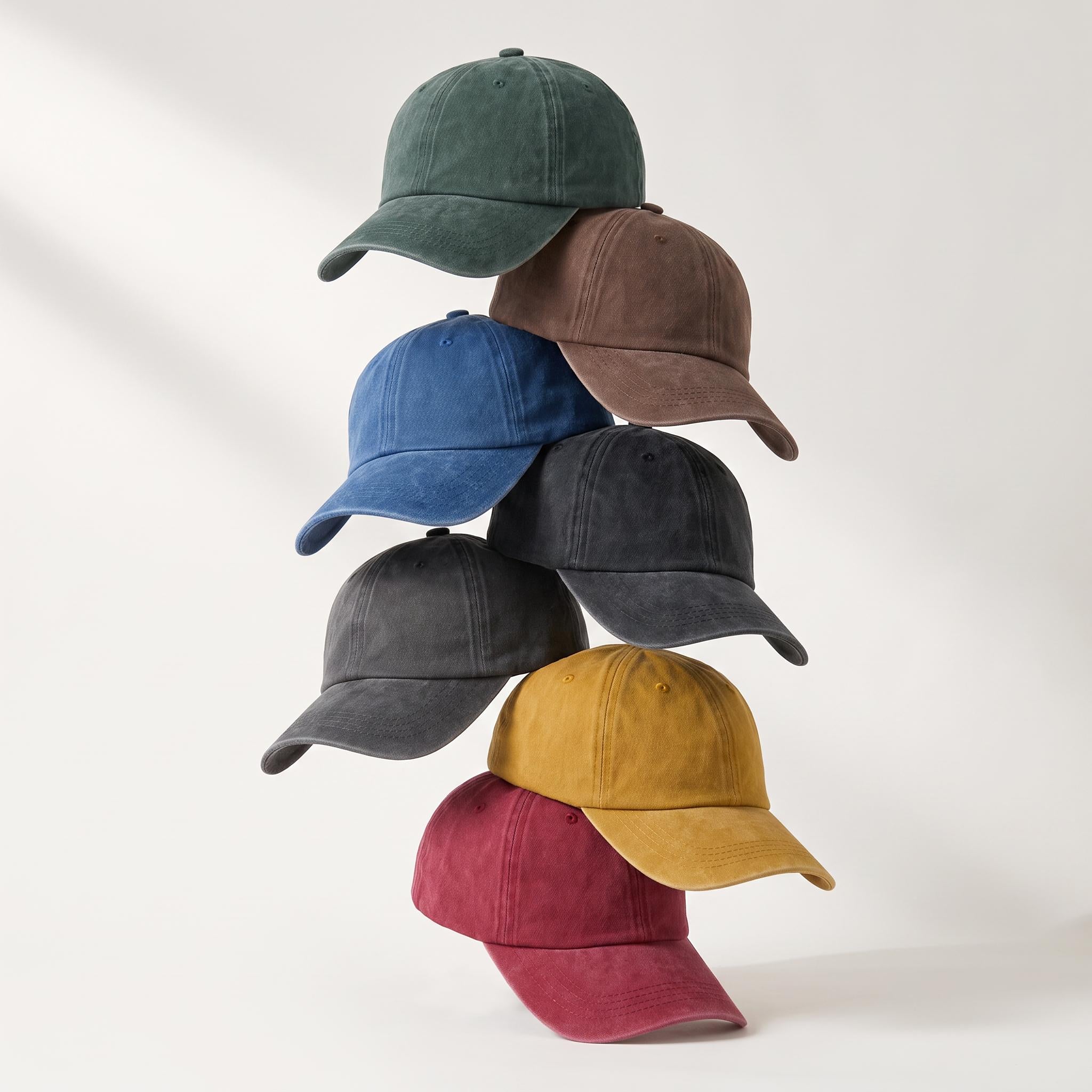 Six baseball caps in different muted colors stacked in a pyramid on a clean white background. The colors include dark green, brown, blue, charcoal gray, mustard yellow, and burgundy.