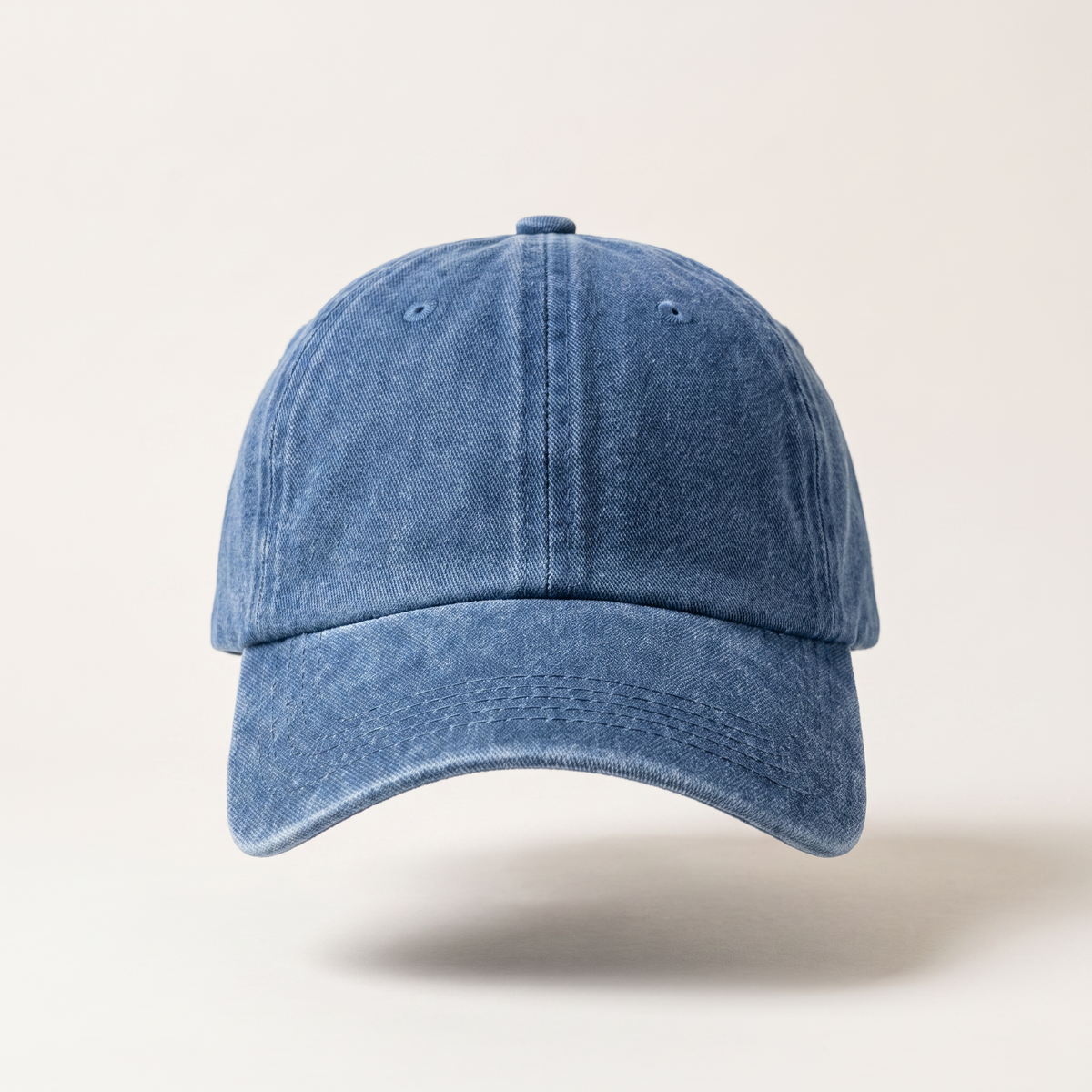 A classic six-panel baseball cap in a washed, distressed medium blue denim-like fabric, shown from a front-facing perspective against a light beige background.