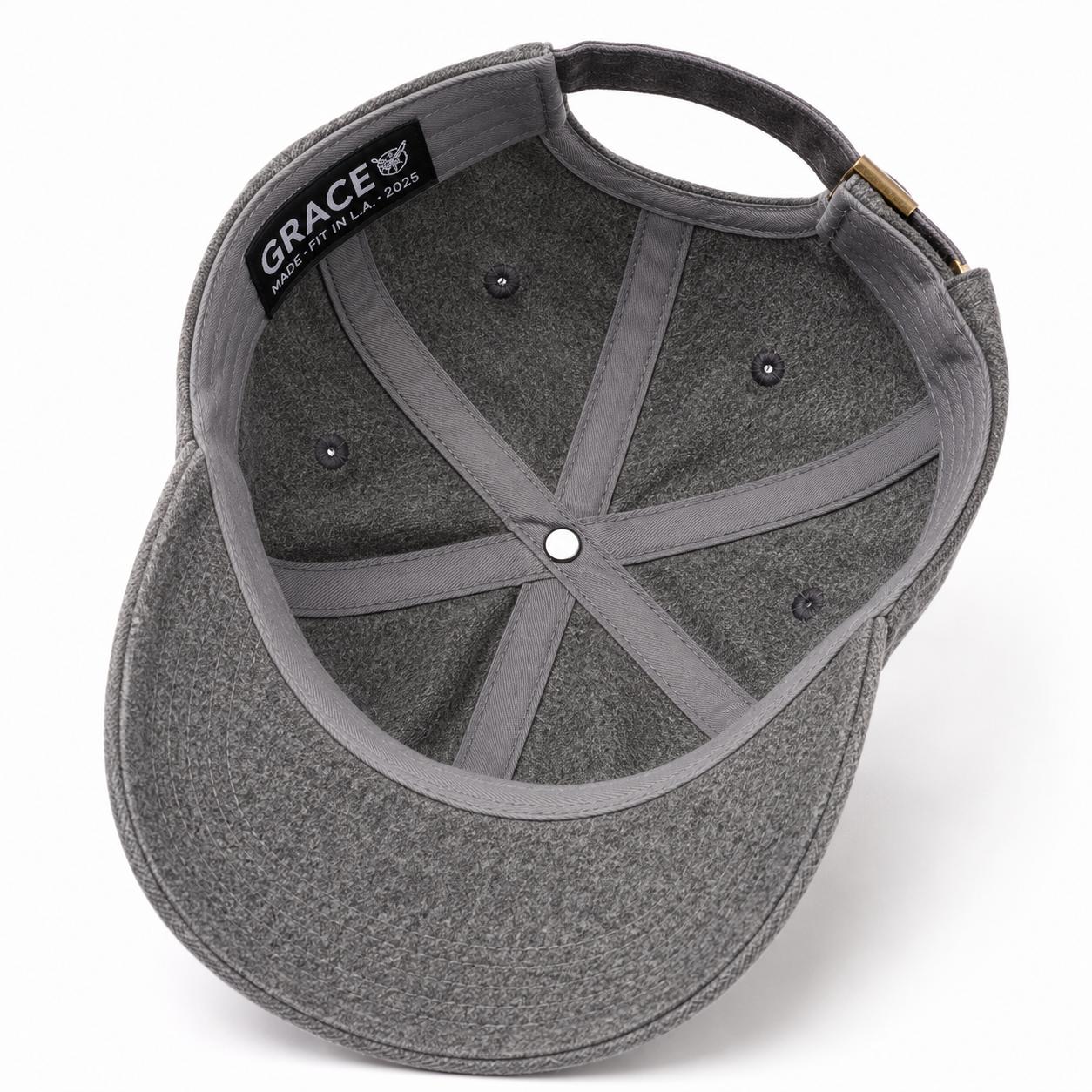 The interior view of a dark gray felt baseball cap, showing the curved brim, internal stitching, and a black fabric label on the crown that reads 'GRACE' with a bear logo.