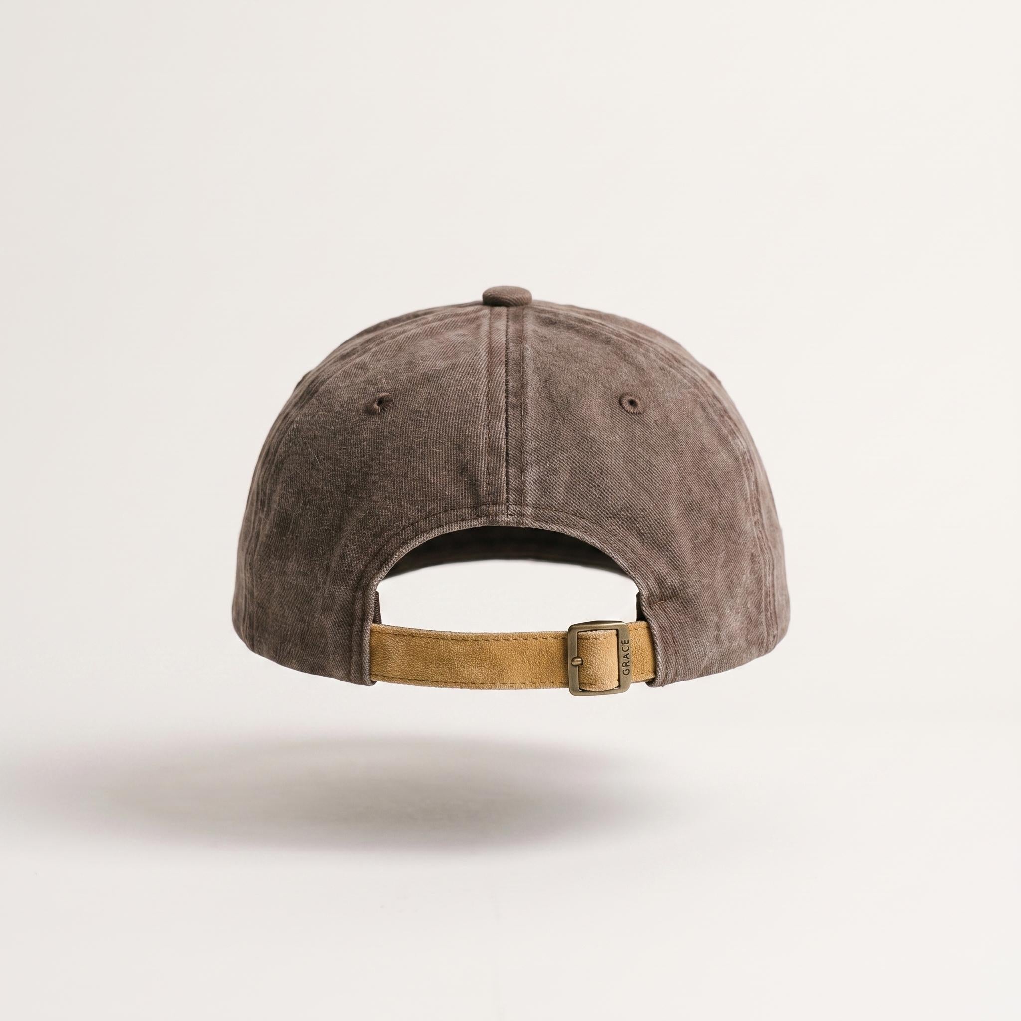 A washed brown baseball cap shown from the back, featuring a tan adjustable strap with a metal buckle, photographed against a clean off-white background.