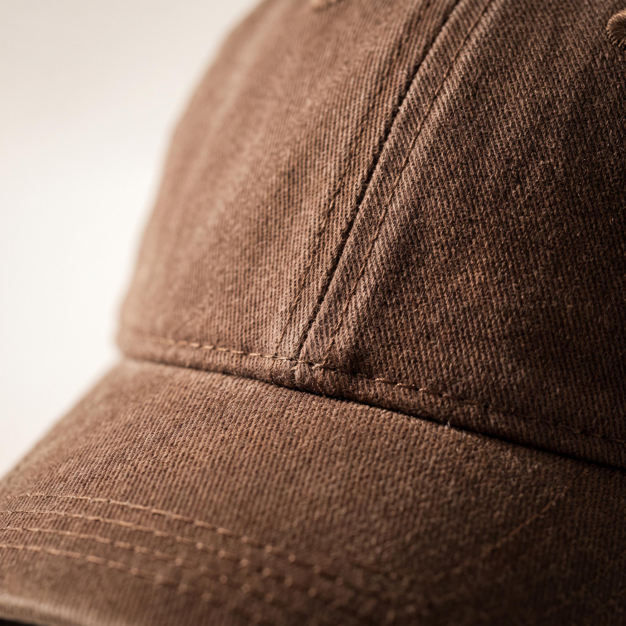 Close-up of a brown cotton twill baseball cap showing the curved brim and stitched panel construction.