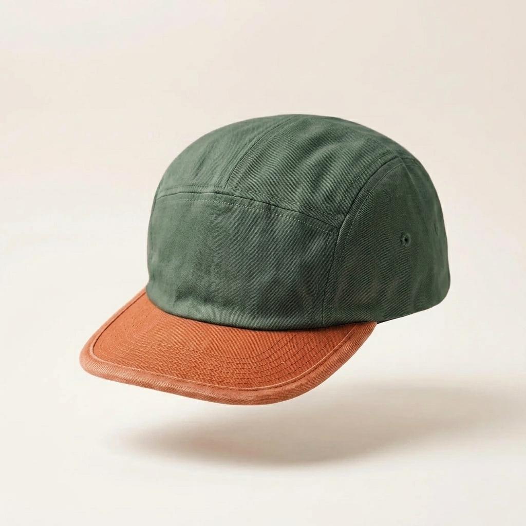 A five-panel camp cap with an olive green crown and a contrasting rust-orange brim, shown floating against a warm off-white background.