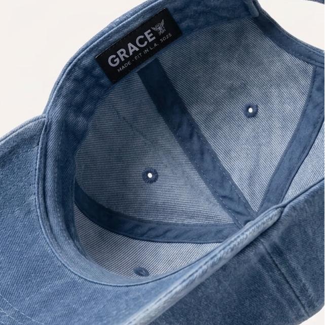 A blue denim baseball cap shown floating at an angle, displaying the interior with a black brand label that reads 'GRACE' and 'MADE IN THE USA'.
