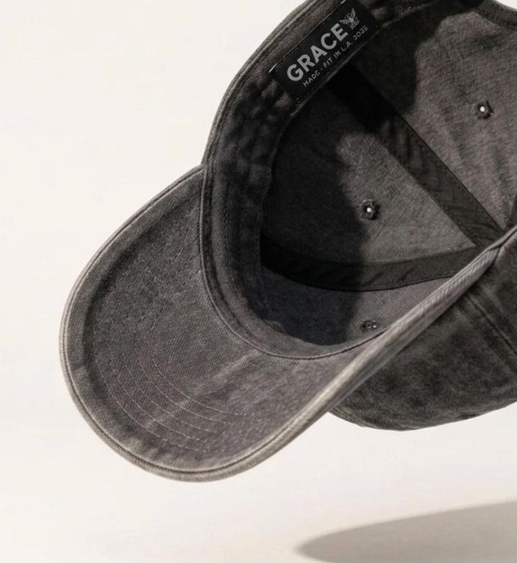 A dark gray washed cotton baseball cap floating at an angle against a clean white background, showing the curved brim, interior crown, and adjustable strap.