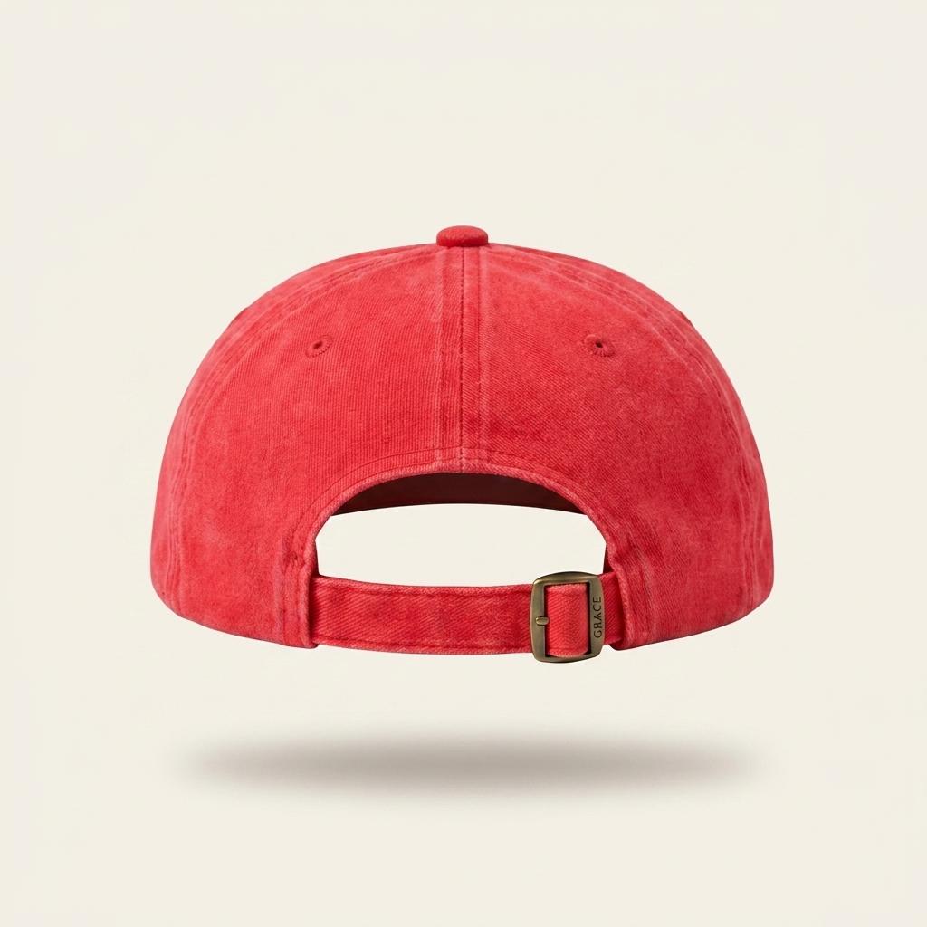 A red washed cotton baseball cap shown from the back, featuring a curved strap and a small metal buckle, set against a light cream background.