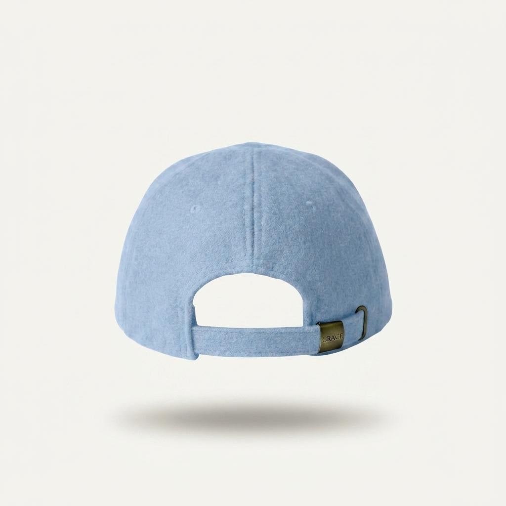 A light blue baseball cap shown from the back, featuring a fabric strap with a small dark metal adjustment buckle, set against a clean off-white background.