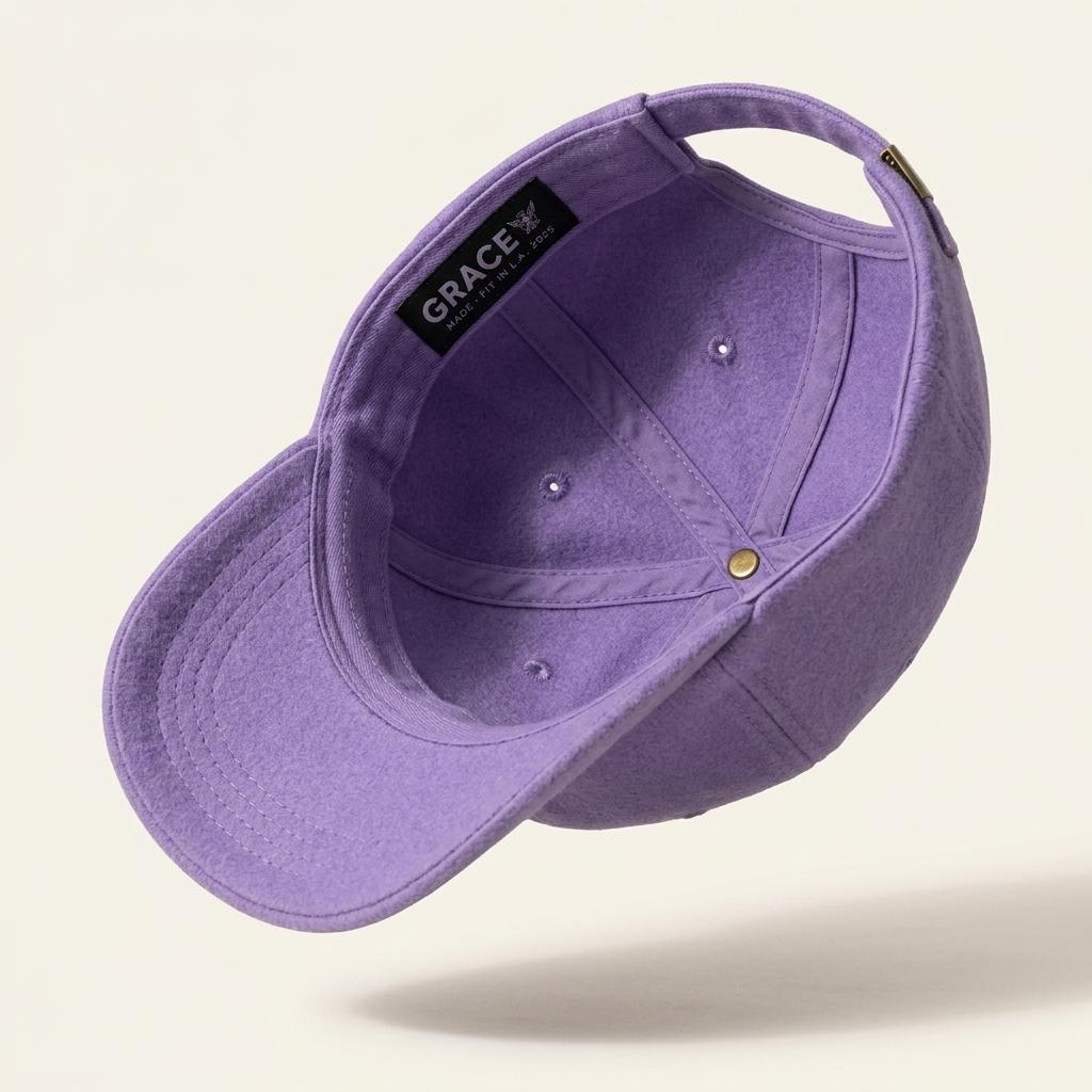 A lavender purple baseball cap shown floating at an angle against a light cream background. The brand name 'GRACE' is clearly visible on the black interior label.