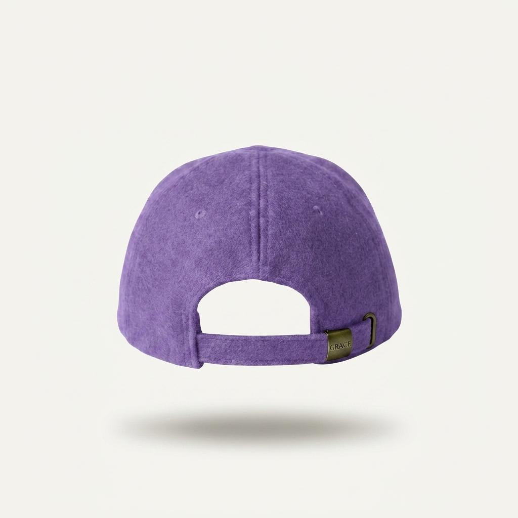 A purple textured baseball cap shown from the back, featuring a fabric strap with a small dark metal adjustment buckle, set against a light off-white background.