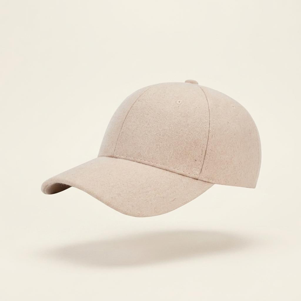 A light beige baseball cap floating against a solid cream background with a soft shadow underneath.