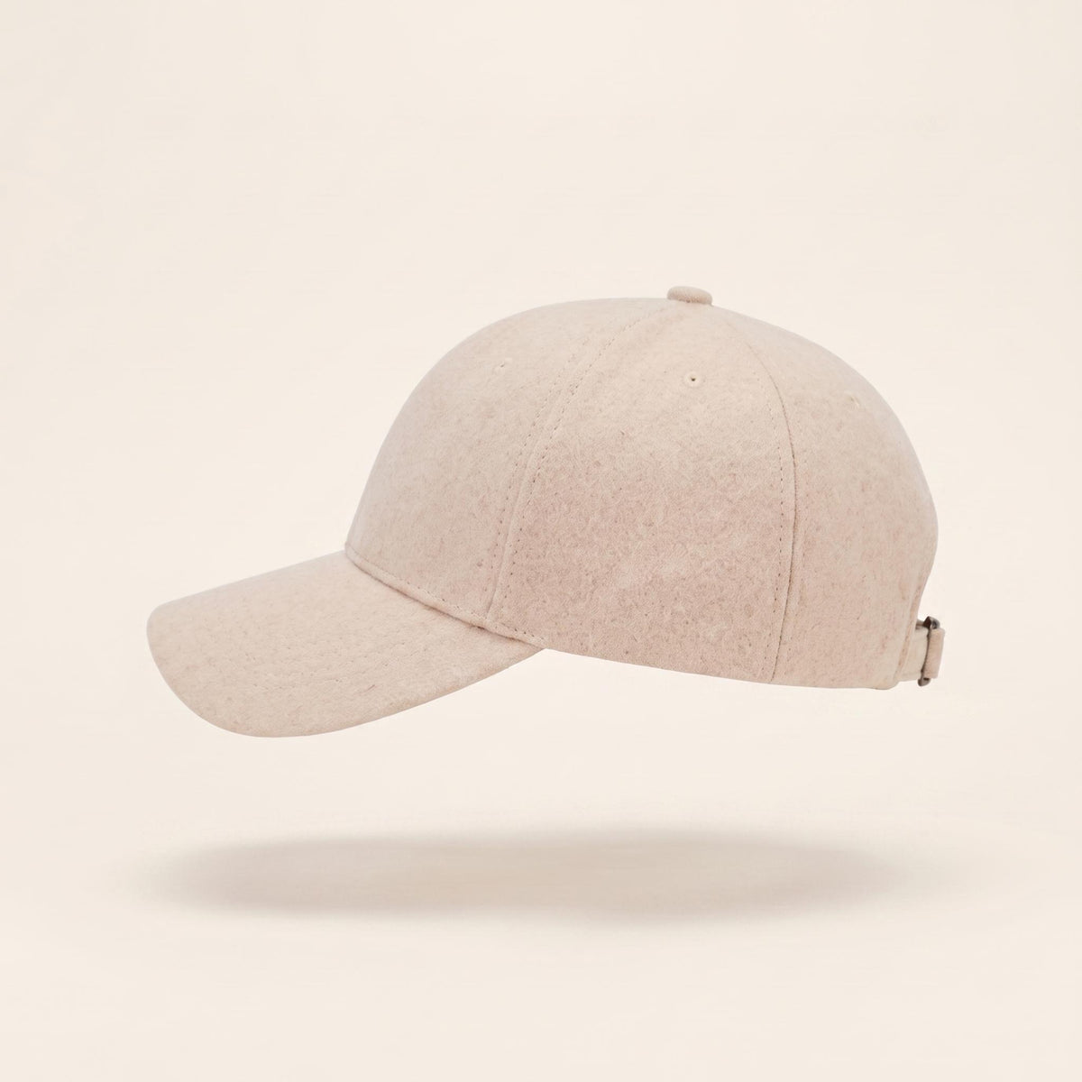 A light beige baseball cap with a curved brim, shown floating against a solid cream background.
