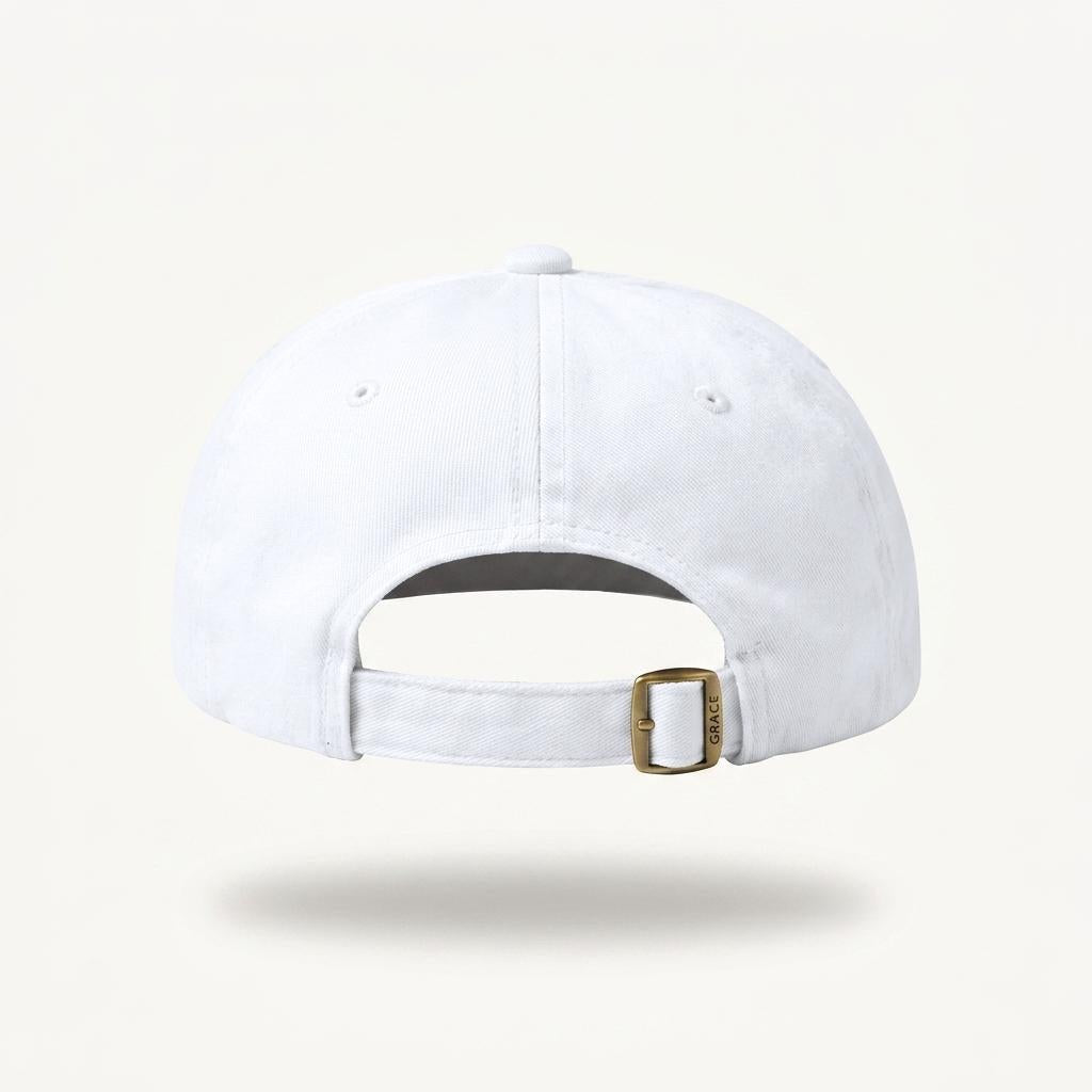 White baseball cap shown from the back, featuring an adjustable fabric strap with a gold-tone metal buckle, set against a light cream background.