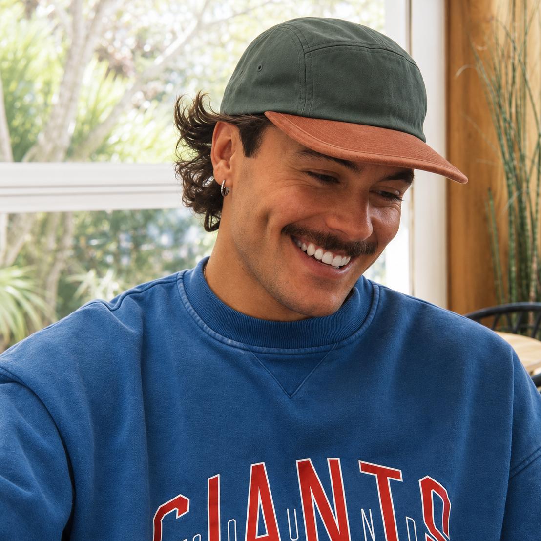 A man wearing a blue sweatshirt with 'GIANTS' printed in red and white, along with a green cap, smiling in a bright indoor setting.